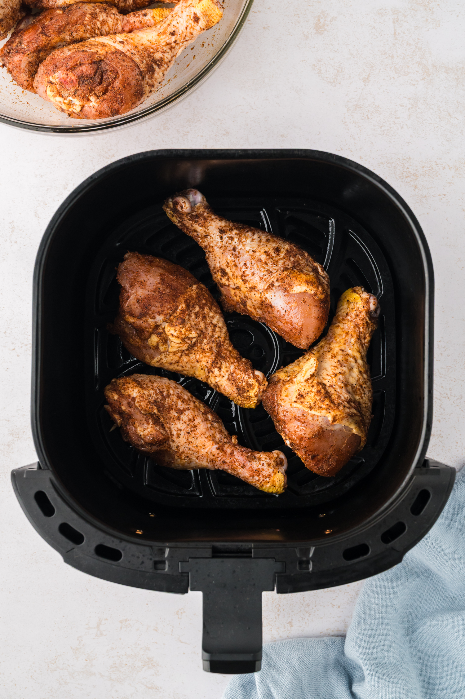 Raw chicken drumsticks are arranged in a single layer inside an air fryer basket.