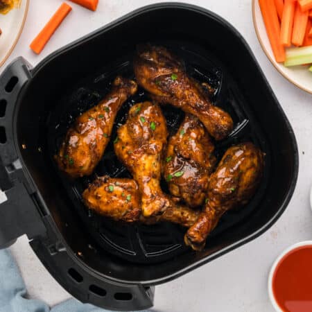 An overhead view shows six buffalo chicken drumsticks arranged in a single layer inside an air fryer basket.