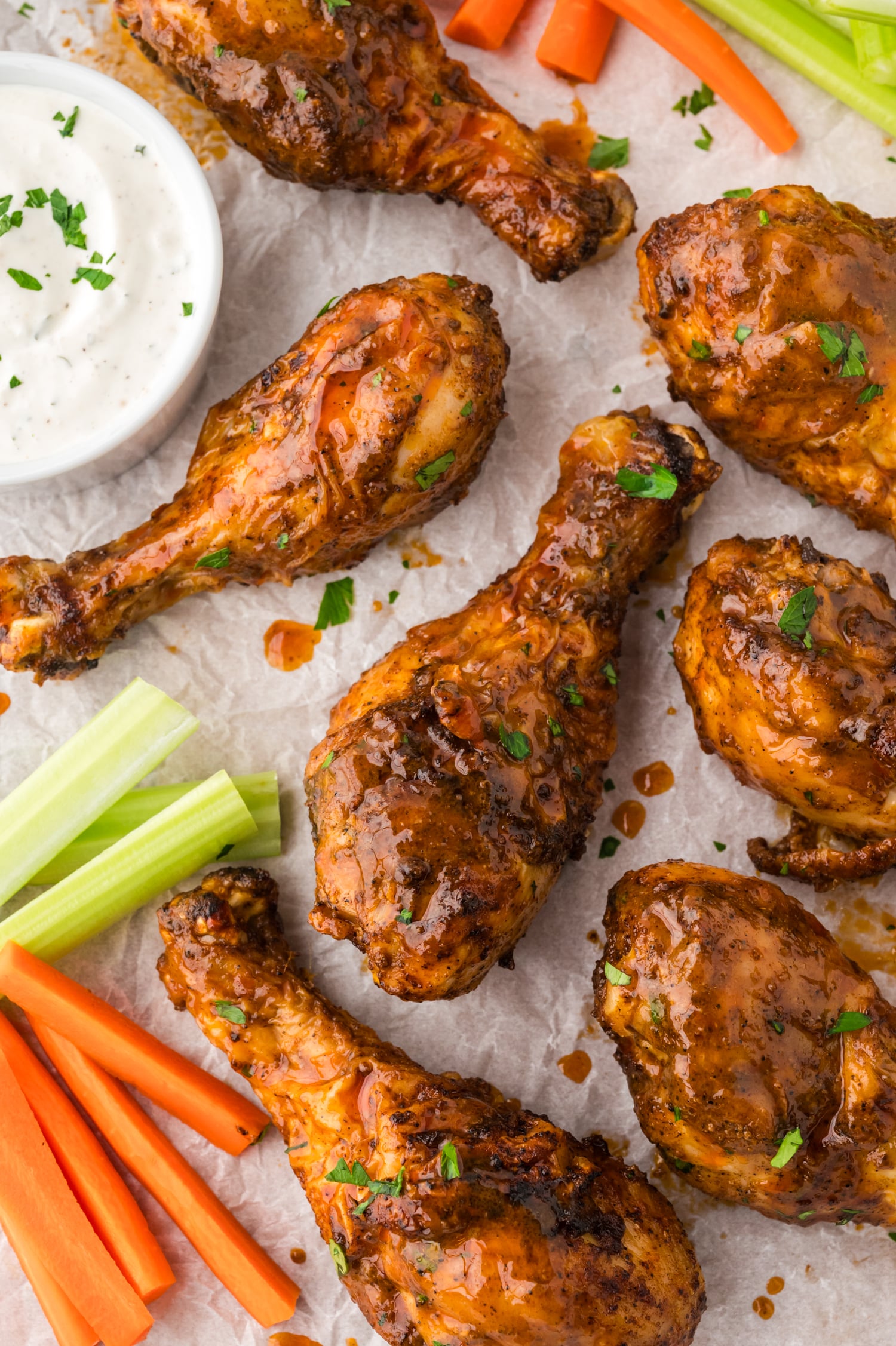 A close-up of buffalo chicken drumsticks resting on parchment paper, their sauce-coated skin glossy and richly colored against the light surface.