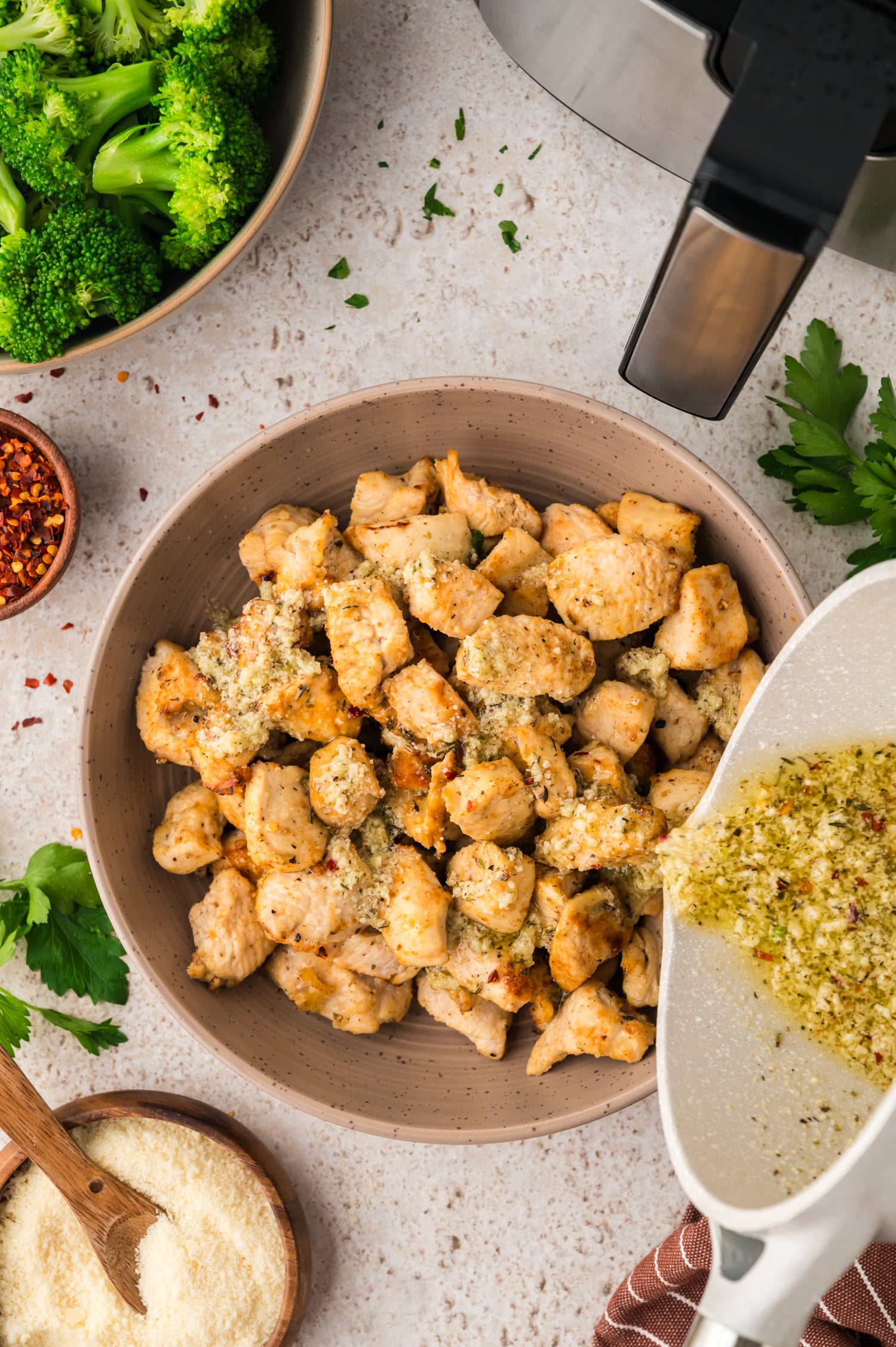 Garlic parmesan seasoning being poured on cooked chicken bites.