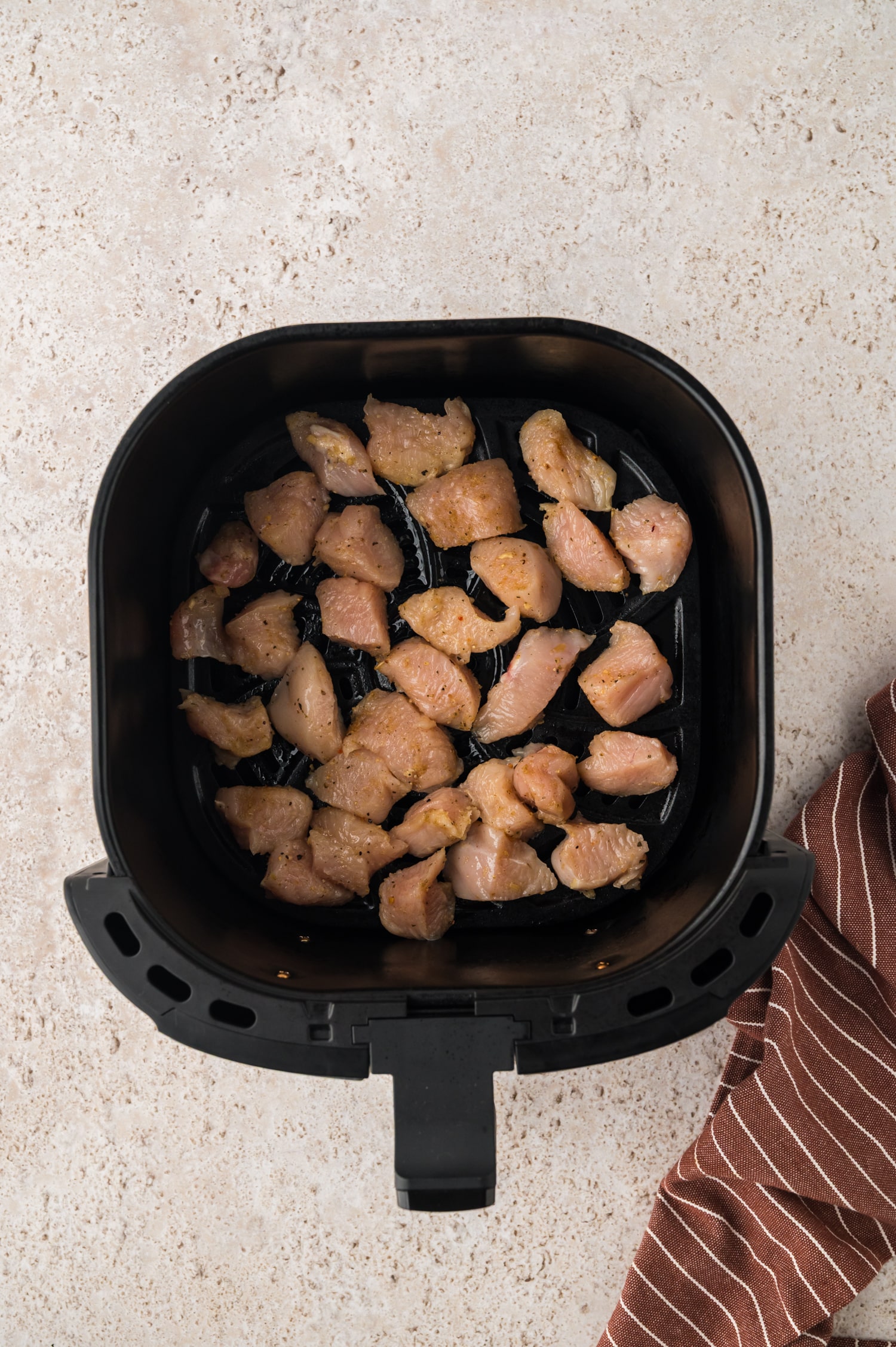 Raw, cut chicken in an air fryer basket.