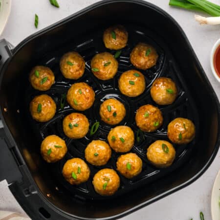 An overhead view of hot honey chicken meatballs arranged in a single layer inside an air fryer basket.