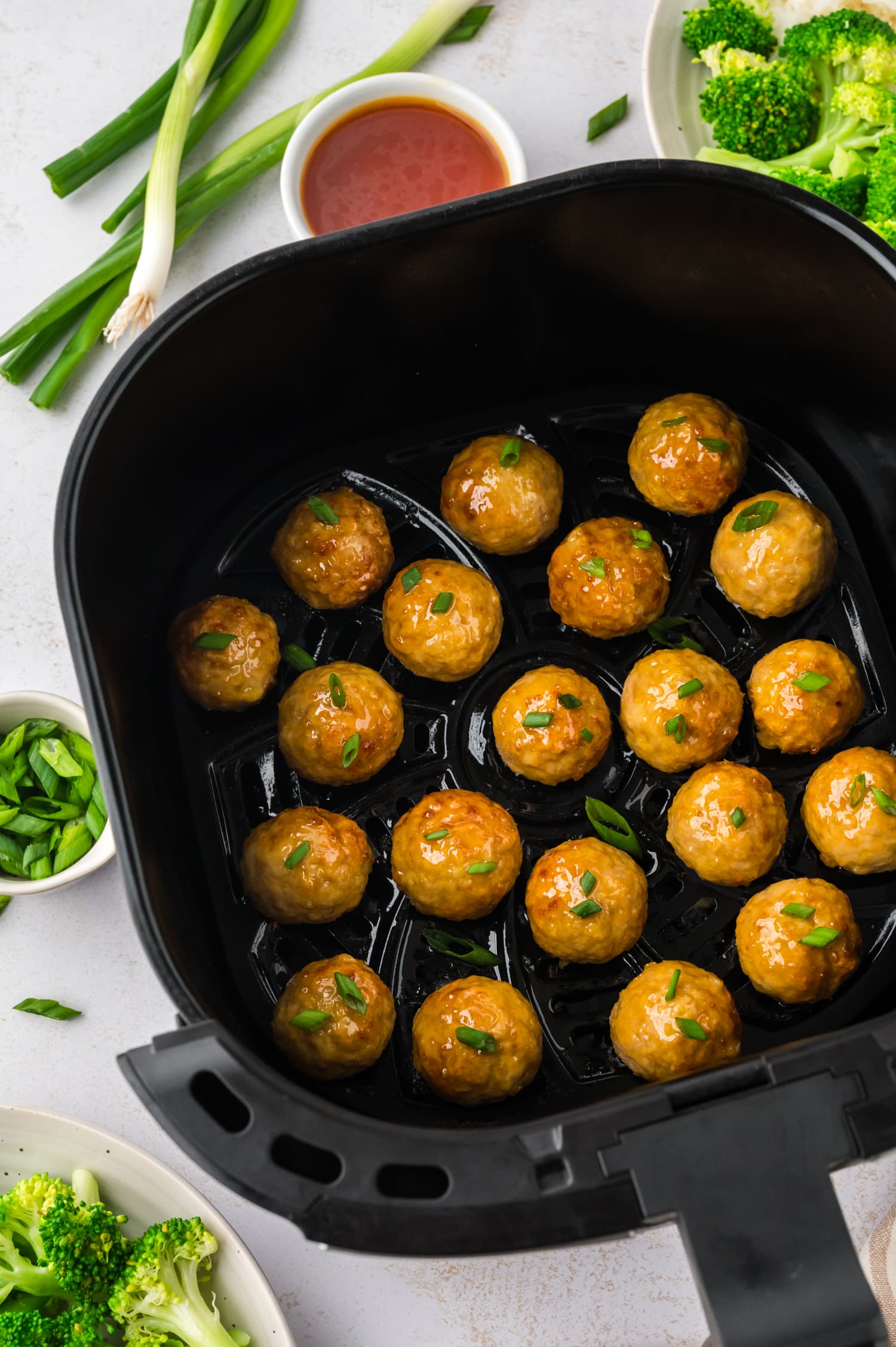 A large batch of hot honey chicken meatballs fills an air fryer basket.