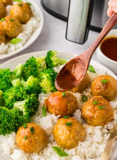 A close-up of a wooden spoon drizzling hot honey over chicken meatballs, coating them in a glossy, sweet layer.