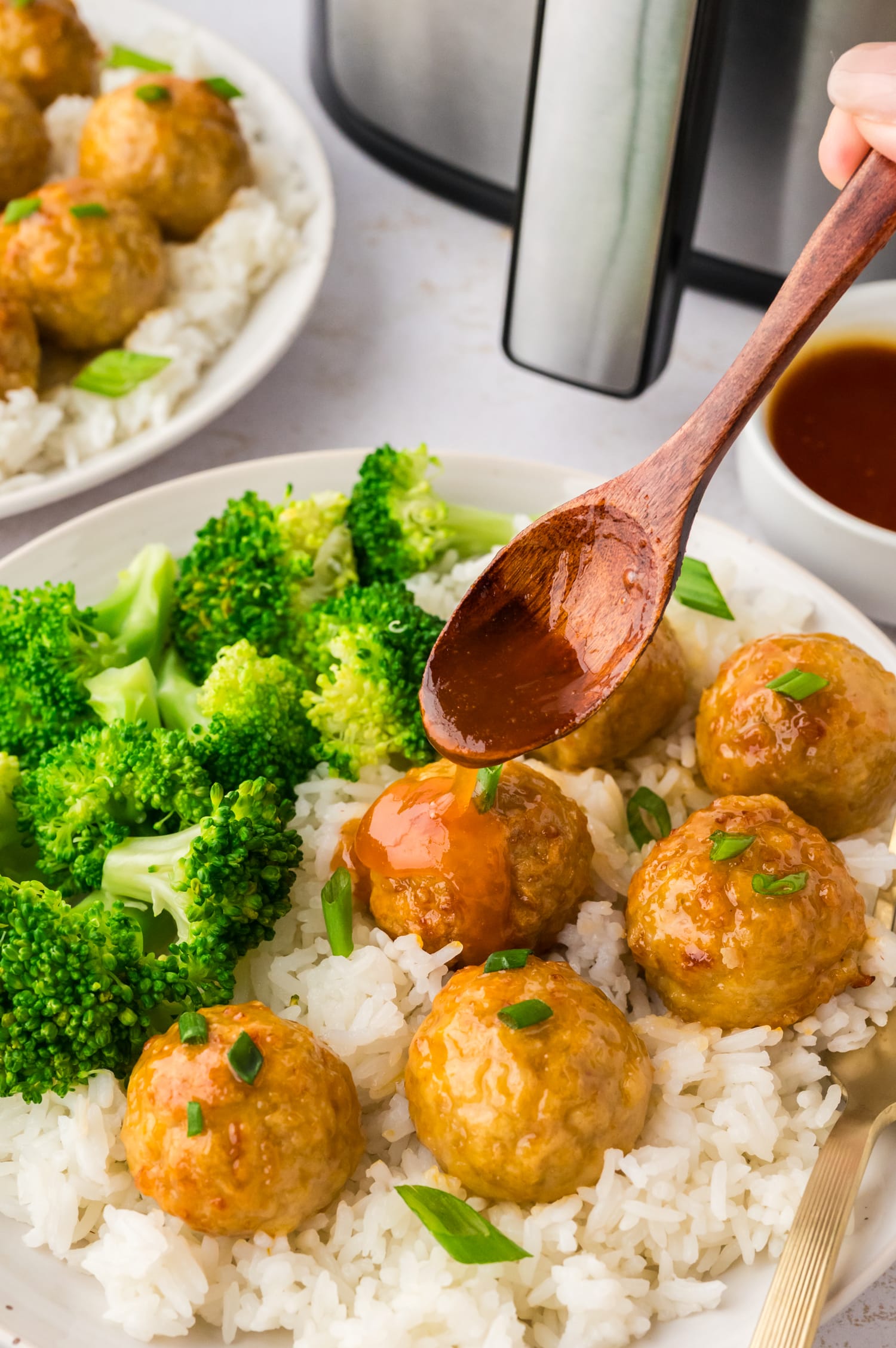 A close-up of a wooden spoon drizzling hot honey over chicken meatballs, coating them in a glossy, sweet layer.