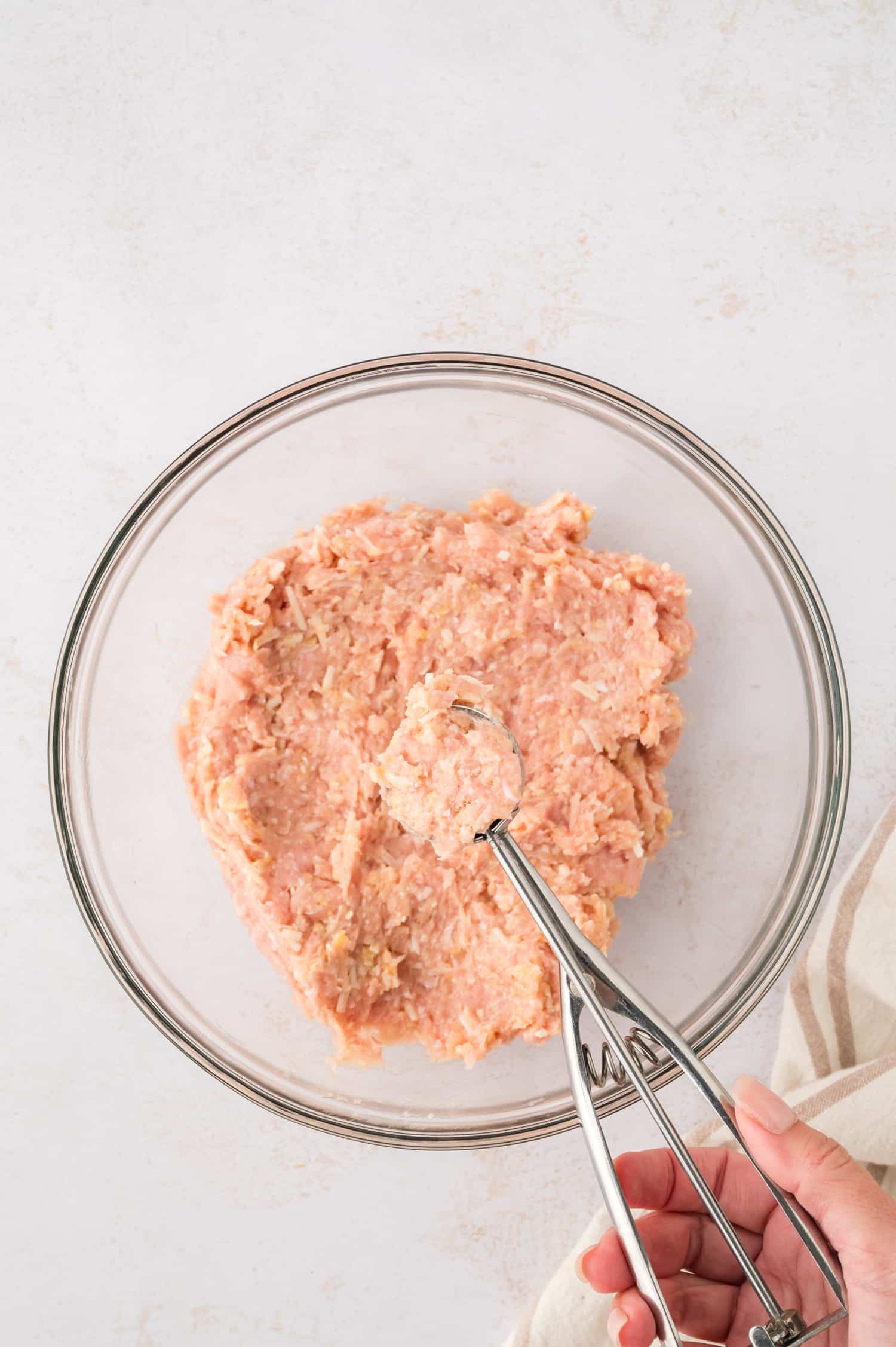 A cookie scoop is being used to portion ground chicken into evenly shaped portions.