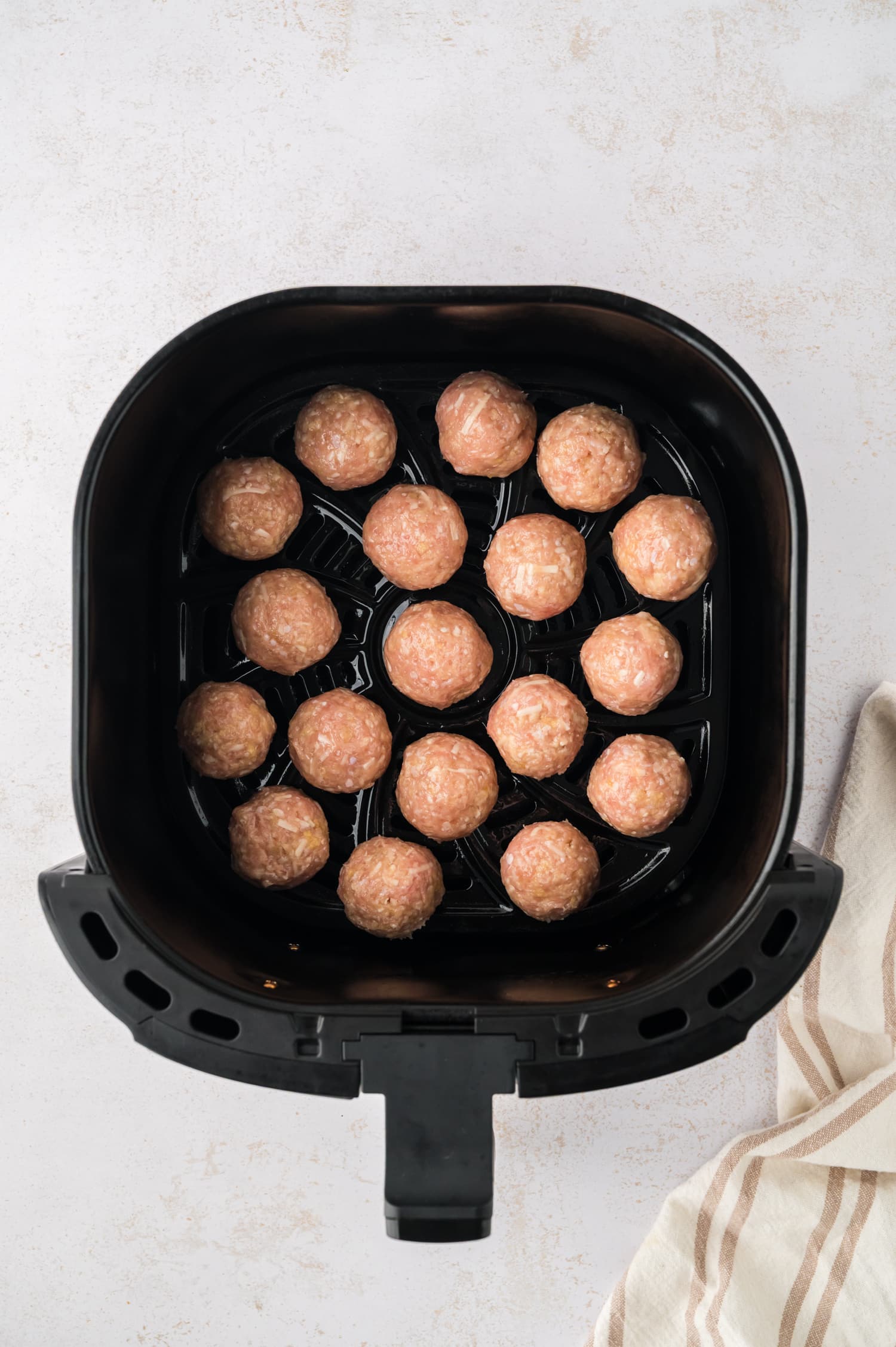 Raw chicken meatballs are arranged in a single layer inside an air fryer basket.