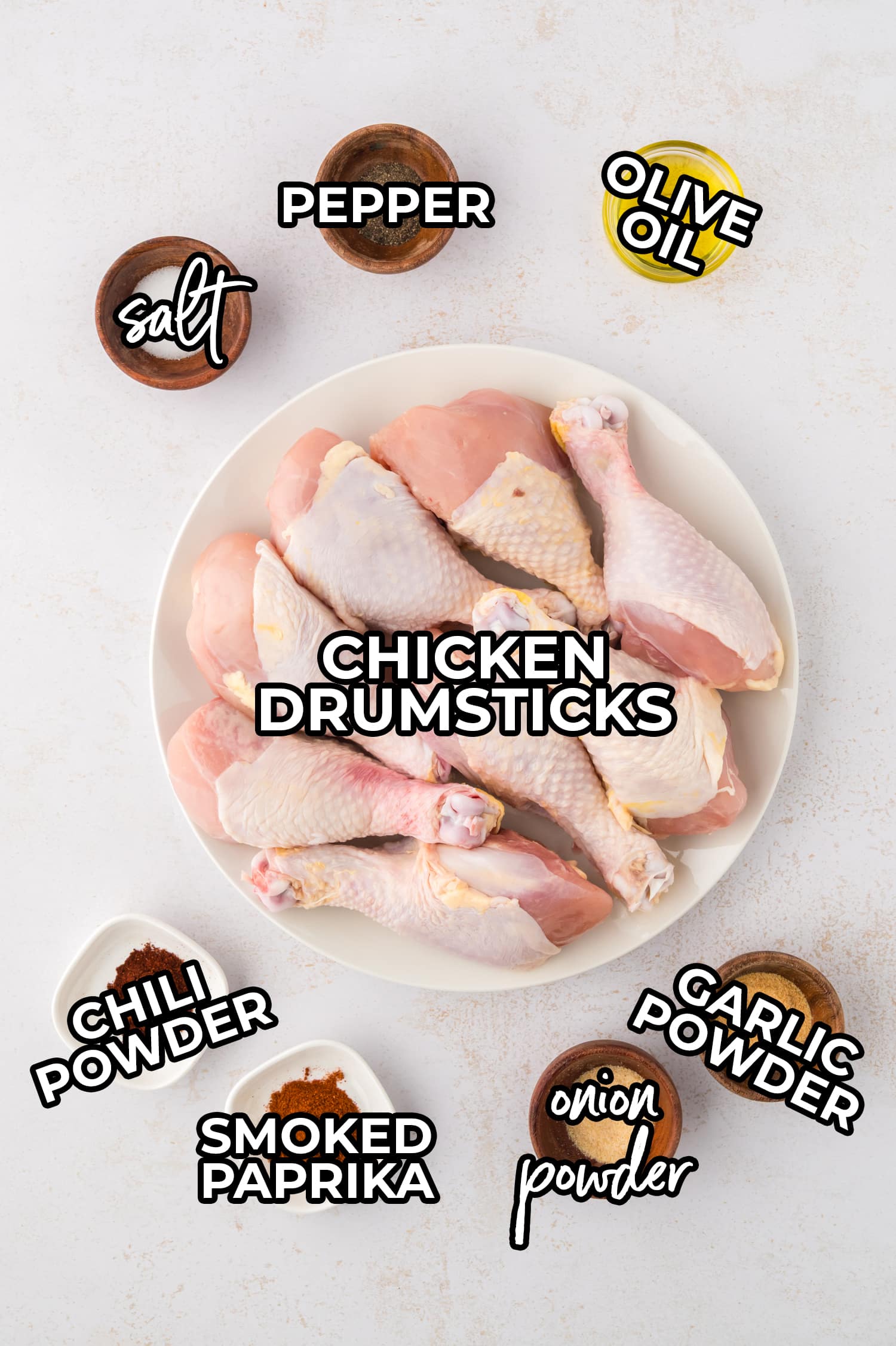 Ingredients for buffalo chicken drumsticks are arranged on a white countertop, each in its own space and labeled with text for clear identification.