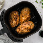 Balsamic chicken breasts are arranged in a single layer inside an air fryer basket.