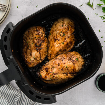 Balsamic chicken breasts are arranged in a single layer inside an air fryer basket.