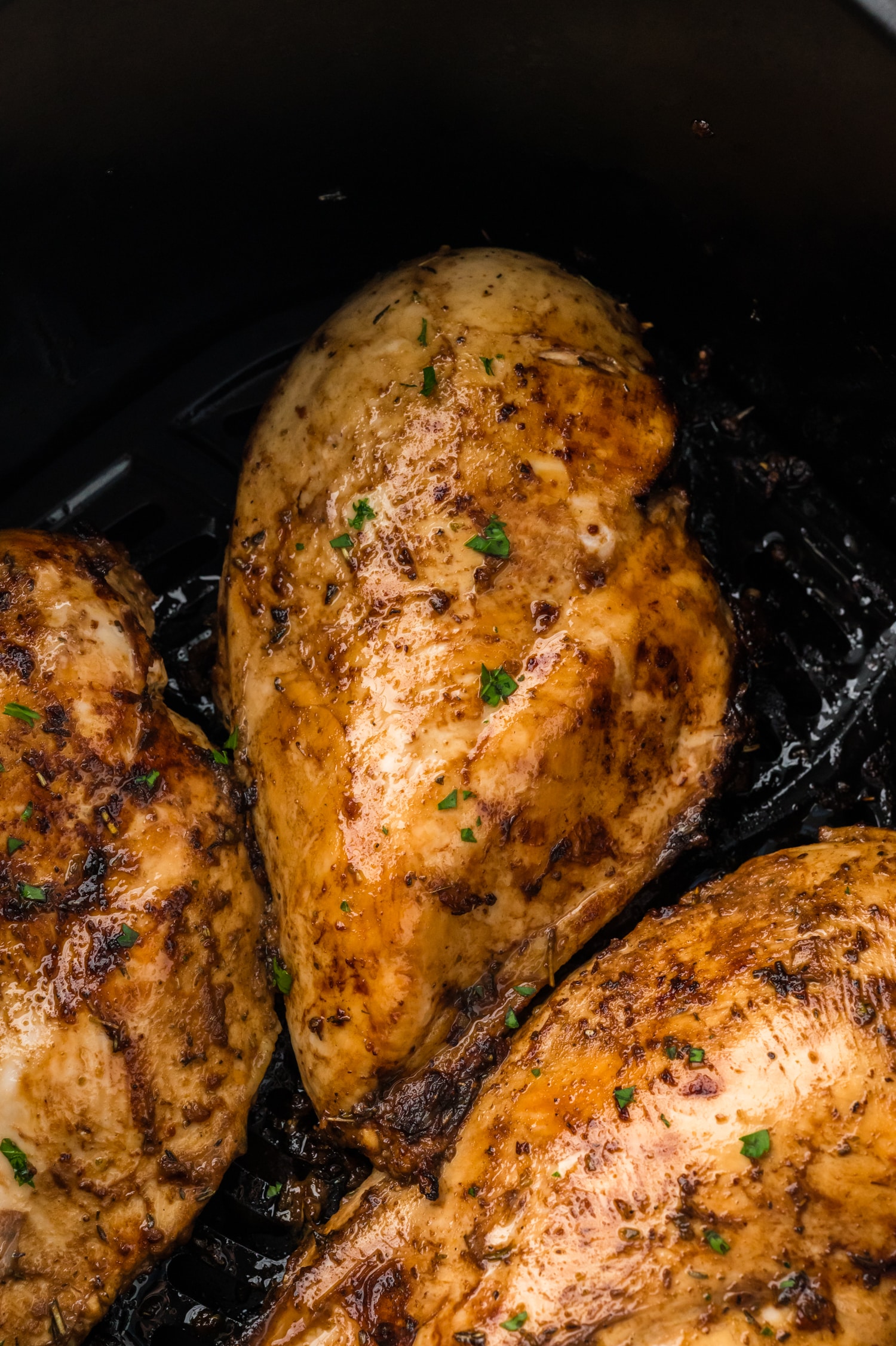 A close-up of a balsamic chicken breast resting in an air fryer basket, showing its glazed, cooked surface.
