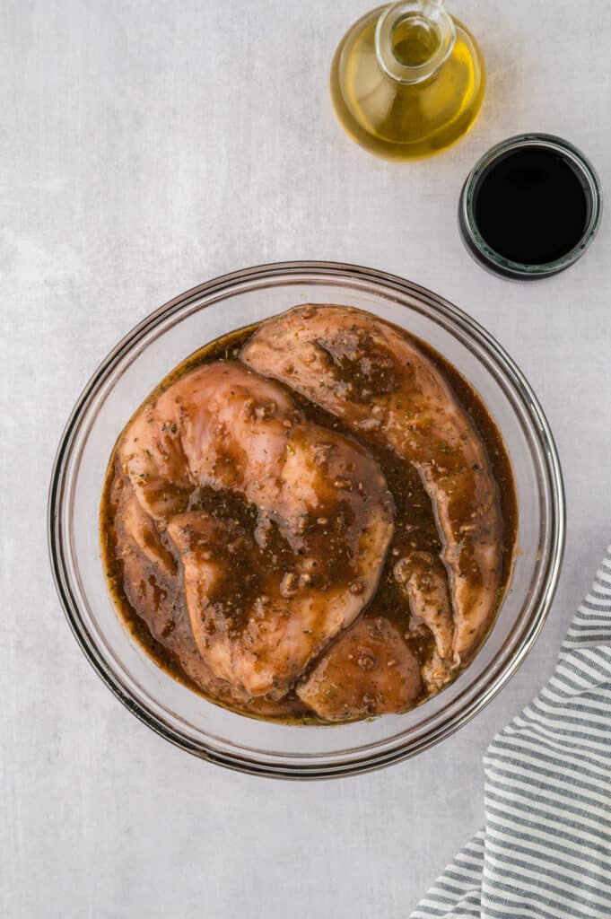Three raw chicken breasts sit next to a clear glass bowl coated with seasoning.