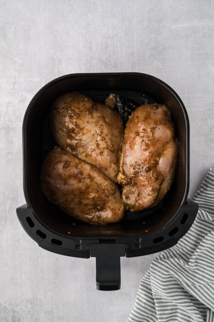 Three raw, seasoned chicken breasts are arranged in a single layer inside an air fryer basket.