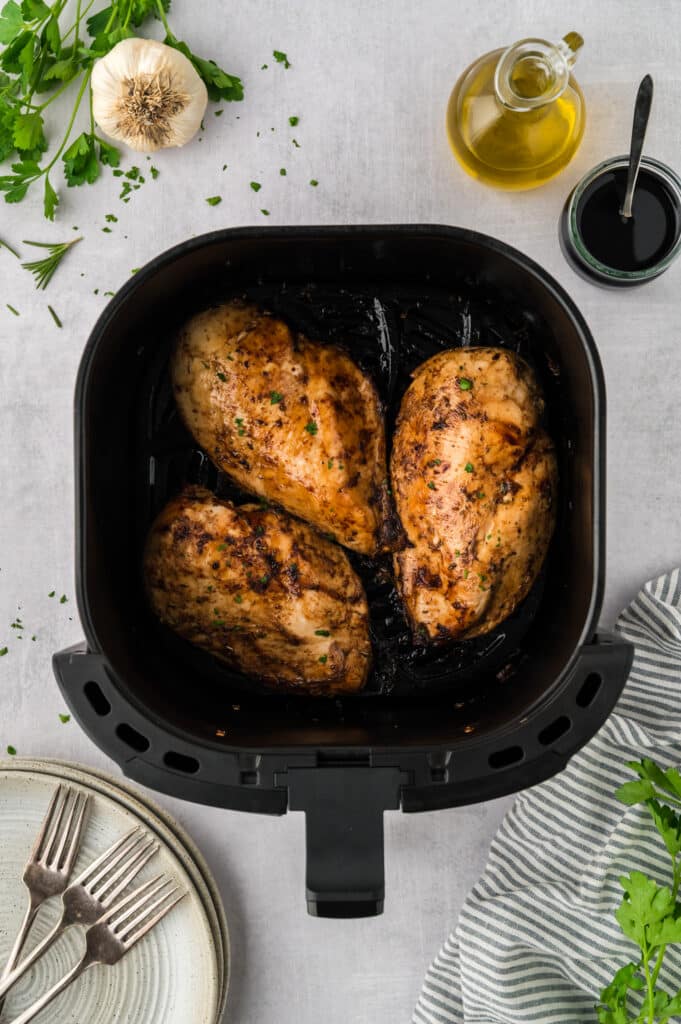 An overhead view of three balsamic chicken breasts arranged in a single layer inside an air fryer basket.