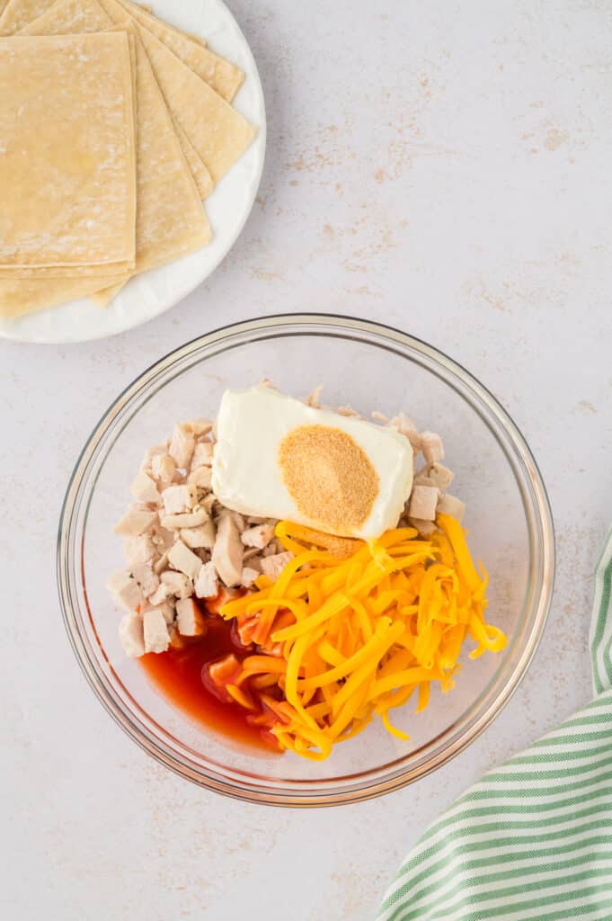 All ingredients for the buffalo chicken wonton filling are combined in a clear glass bowl.