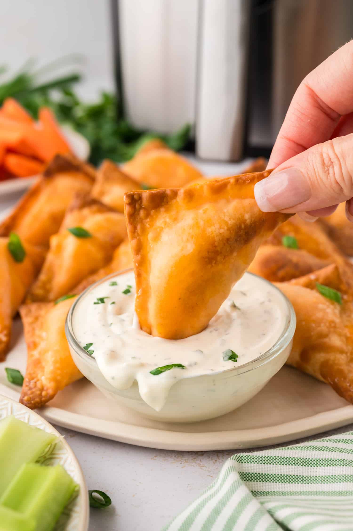 A close-up of a buffalo chicken wonton partially submerged in ranch dressing, with the creamy sauce covering its edge.