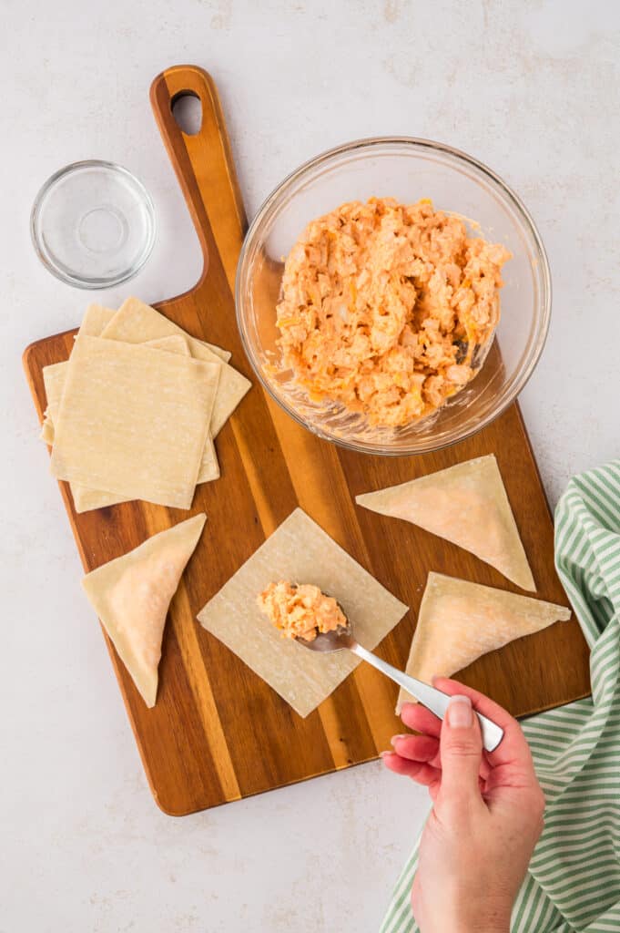 A person uses a spoon to place filling into the center of a wonton wrapper.