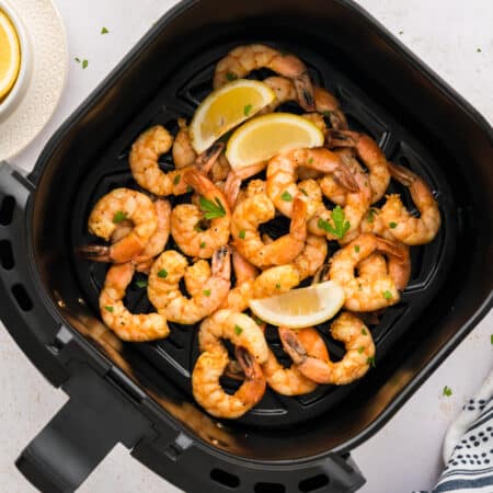 Lemon pepper shrimp in air fryer basket.