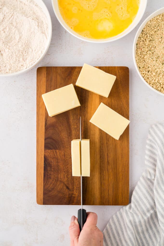 A block of mozzarella cheese is being cut on a wooden cutting board.