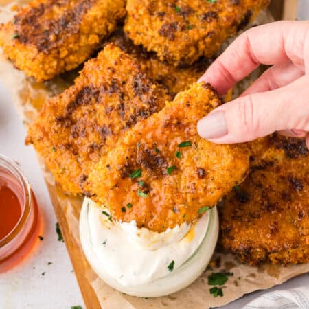 A woman’s hand holds a Nashville hot mozzarella stick as it is dipped into a cup of ranch dressing.