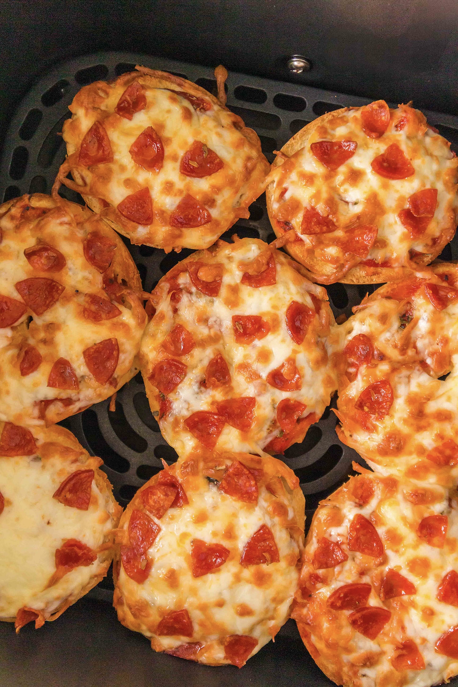 Eight bagel pizzas are arranged in a single layer inside an air fryer basket.