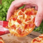 A close-up of a person holding a bagel pizza, showing the toppings and melted cheese on the surface.