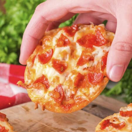 A close-up of a person holding a bagel pizza, showing the toppings and melted cheese on the surface.
