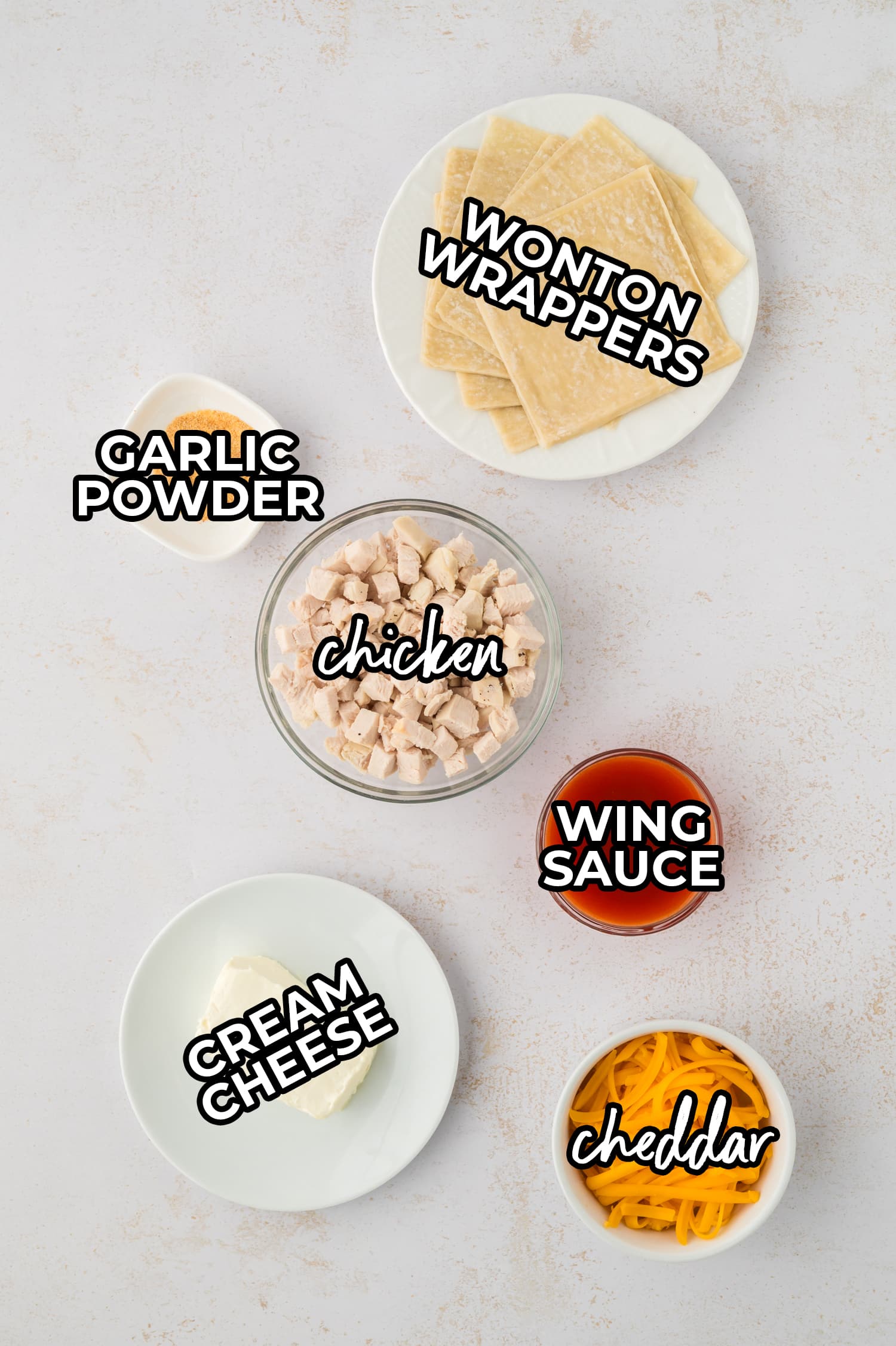 Ingredients for buffalo chicken wontons are arranged on a white countertop, each labeled for clear identification.