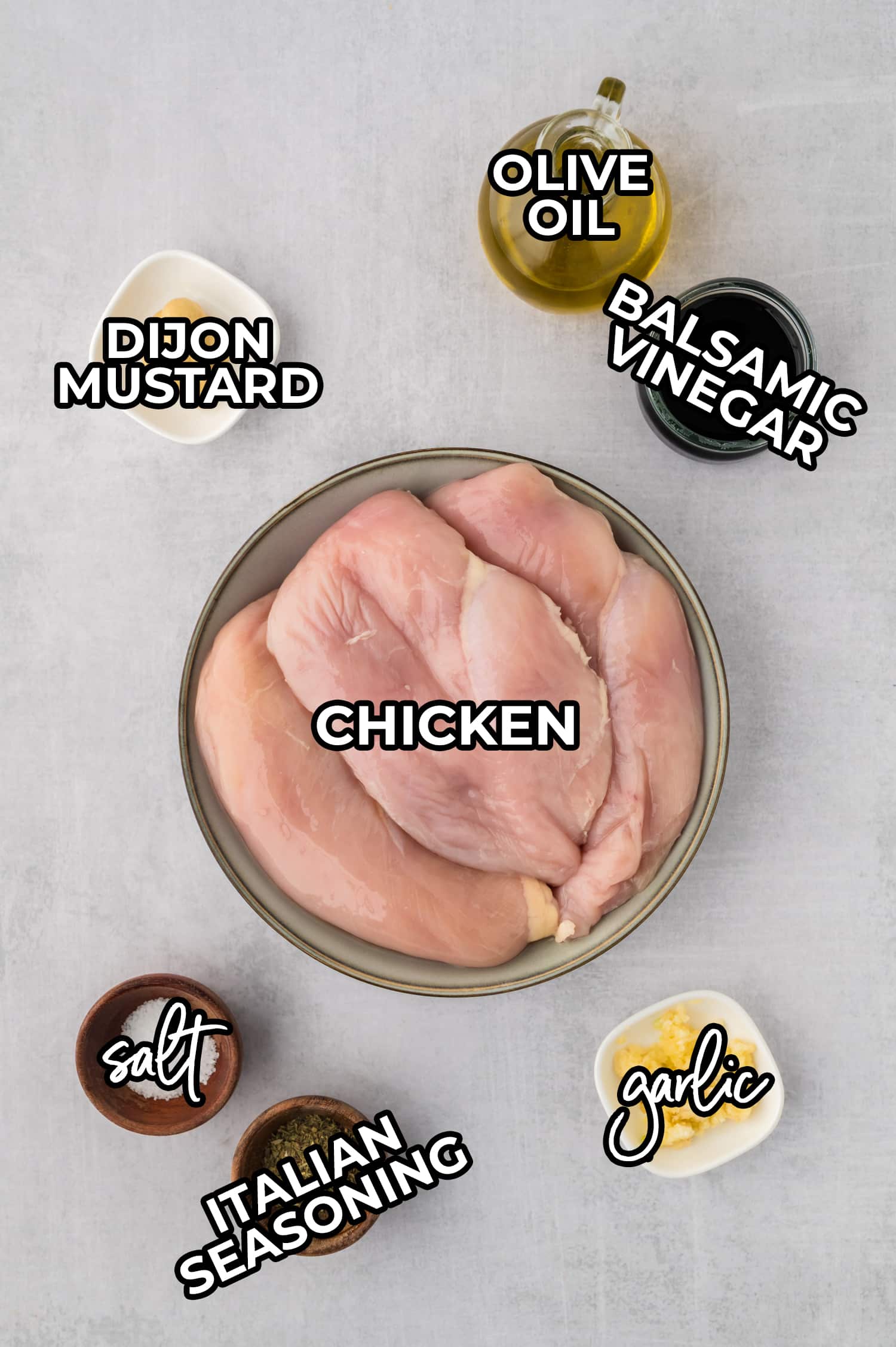 Ingredients for balsamic chicken are arranged on a white countertop, each labeled for clear identification.