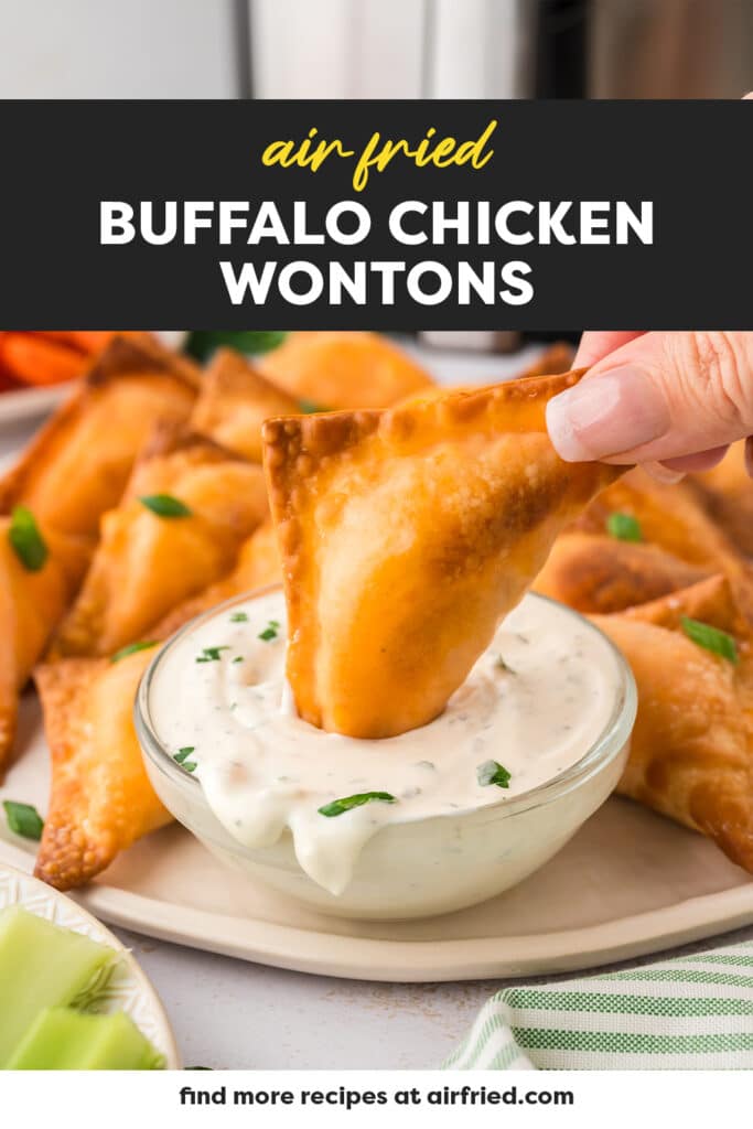 A close-up of a woman dipping a buffalo chicken wonton into a cup of ranch dressing, the creamy sauce coating part of the wonton.