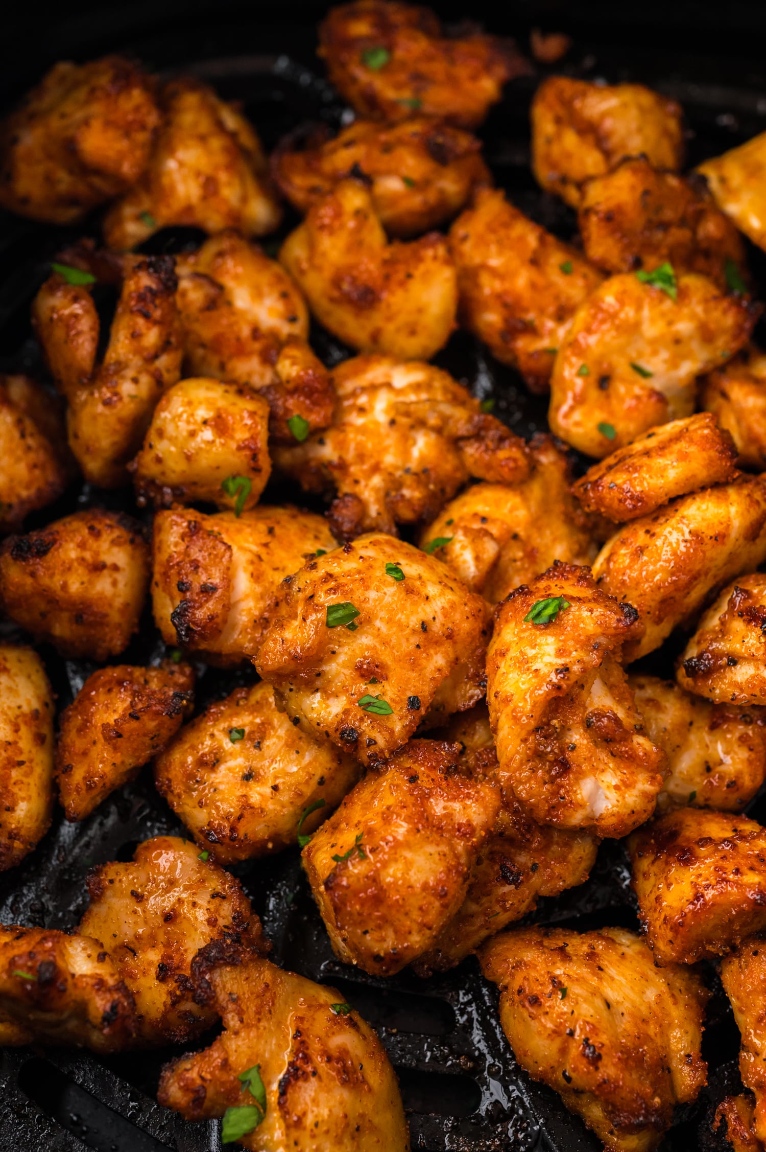Close up of chicken bites in an air fryer basket.