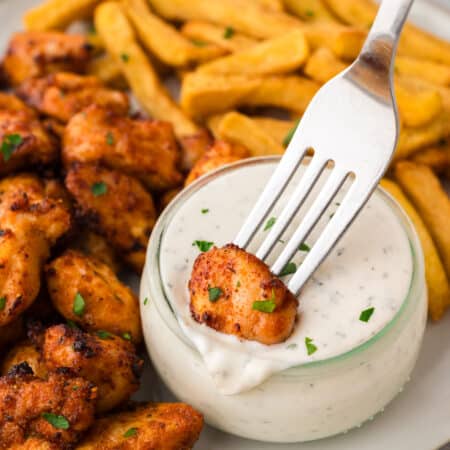Close up of a fork dipping a chicken bite into ranch dressing.