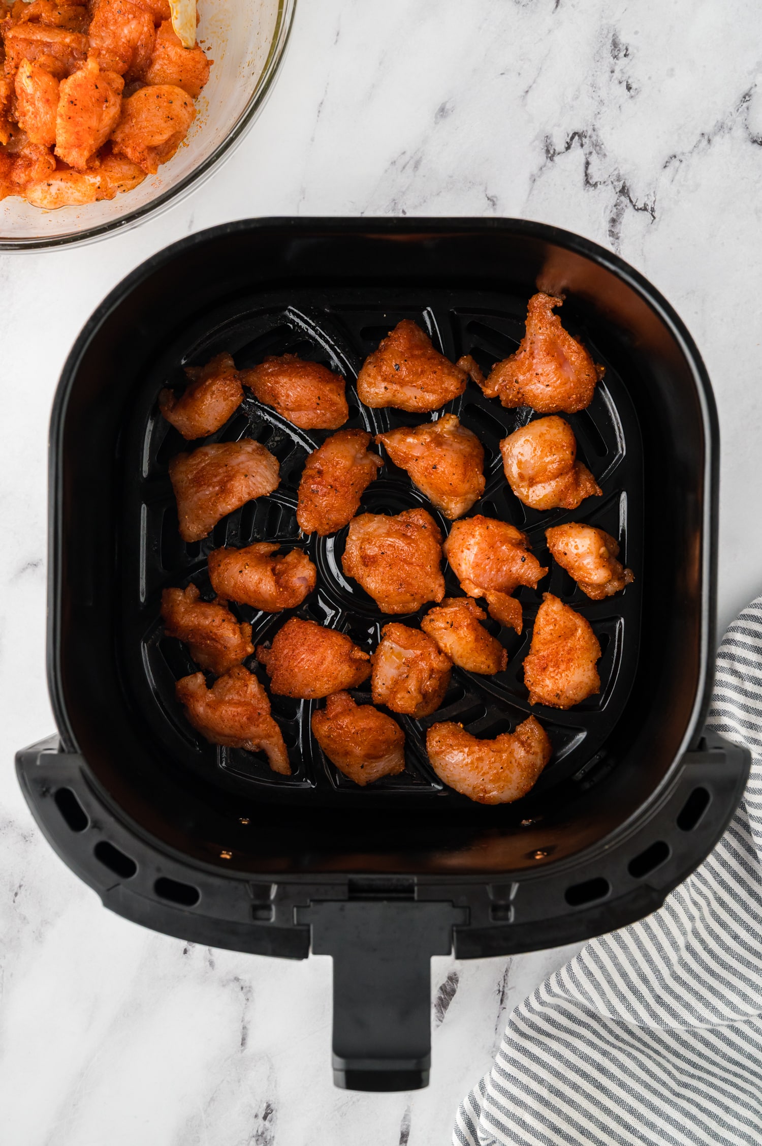 Raw chicken bites spread out in an air fryer basket.