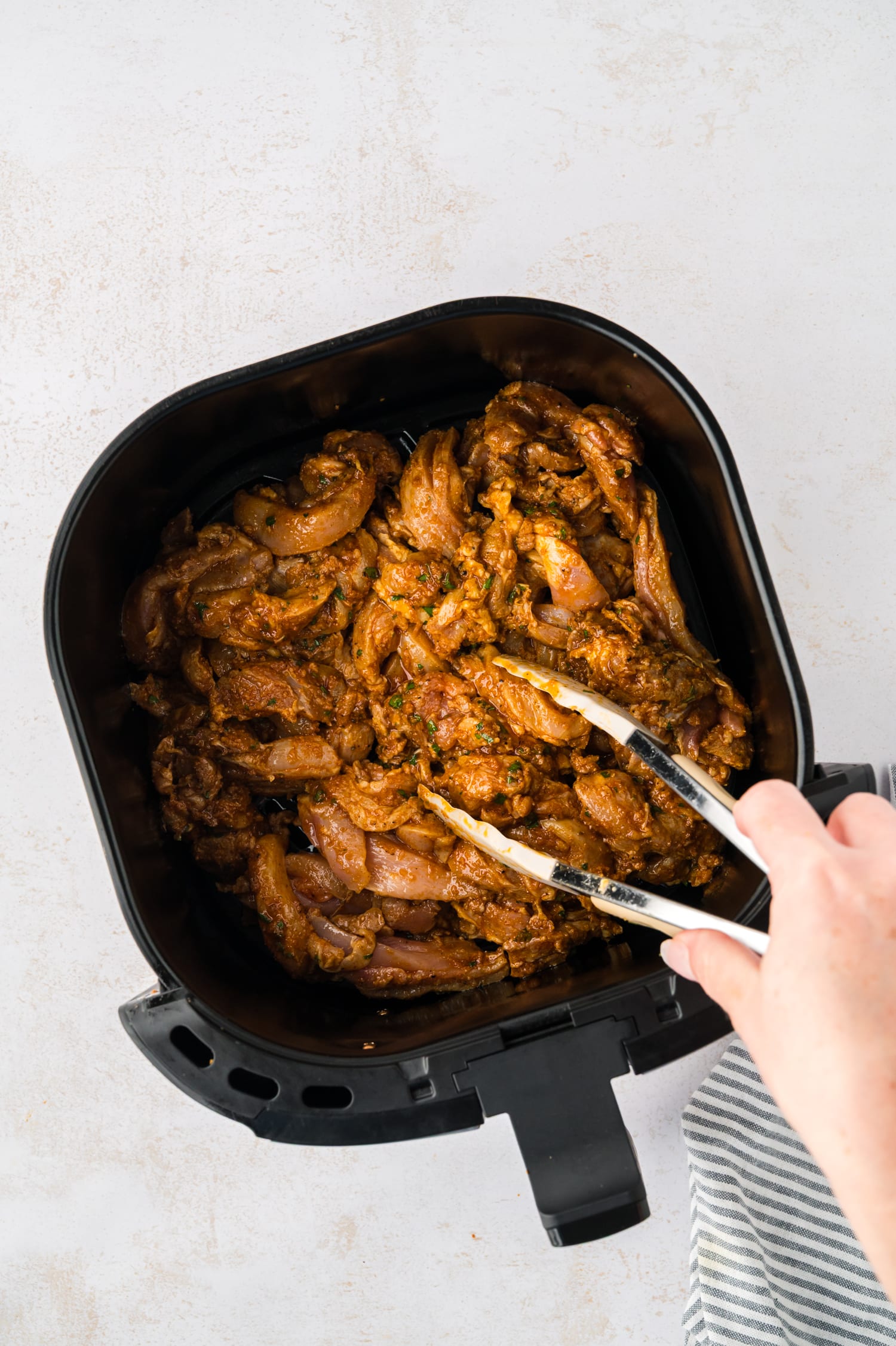 Seasoned raw chicken in an air fryer basket.