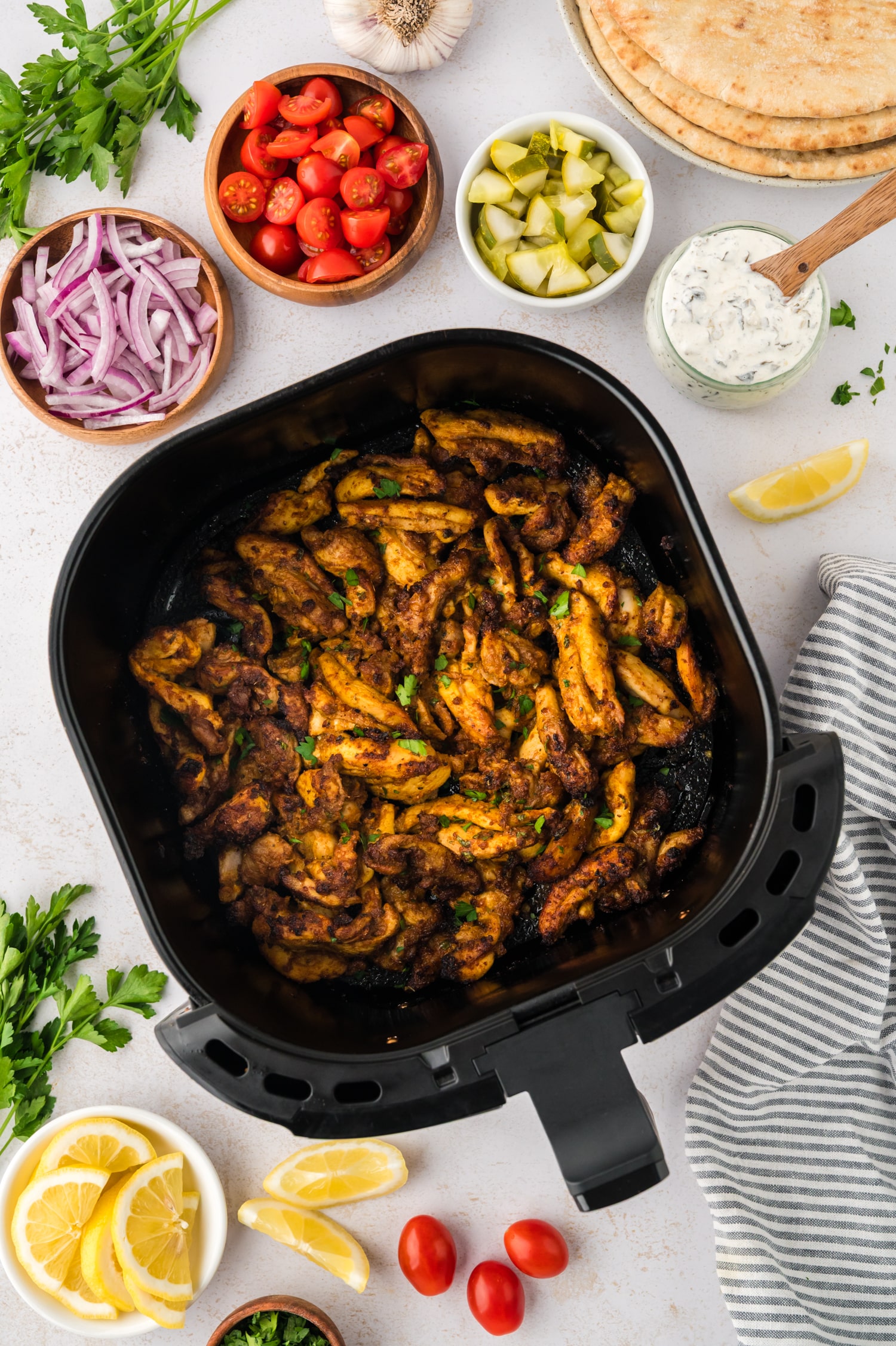 Overhead view of chicken in an air fryer basket surrounded by shawarma toppings.