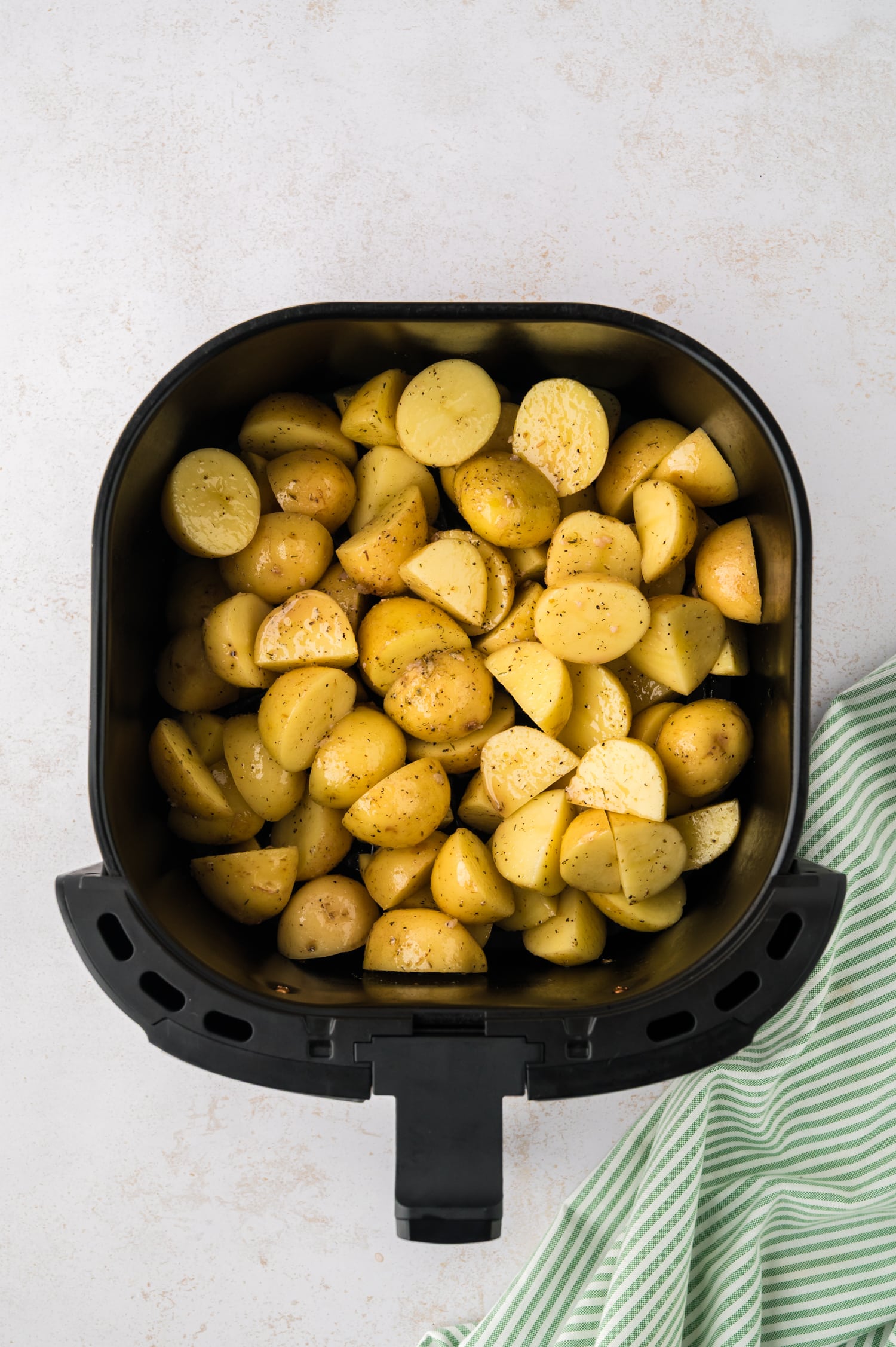 Raw cut and seasoned potatoes in an air fryer basket.