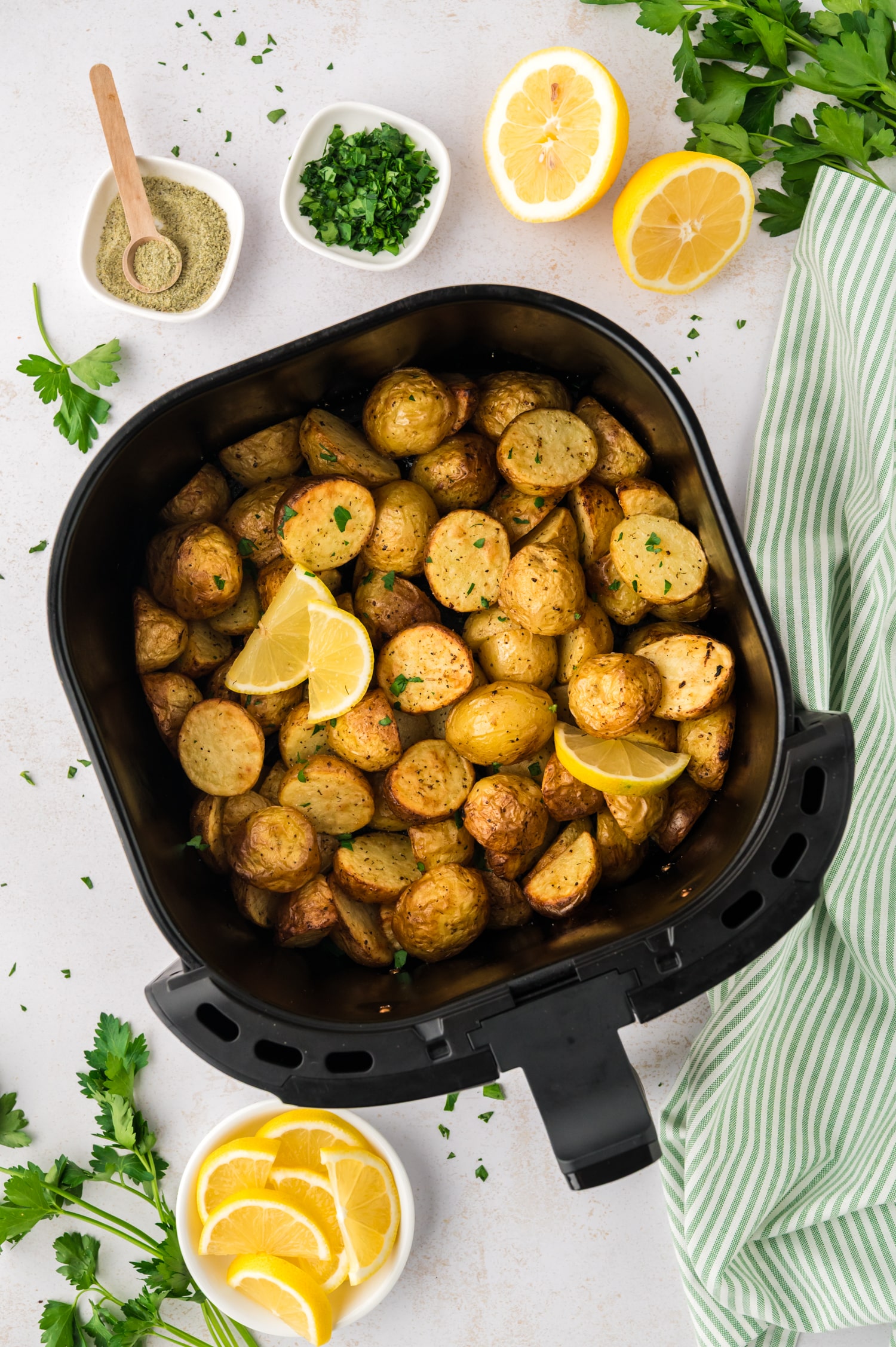 Overhead view of an air fryer basket full of Greek potatoes on a white countertop.