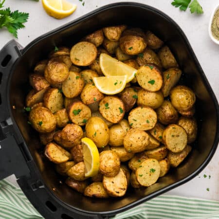Overhead view of Greek potatoes in an air fryer basket.