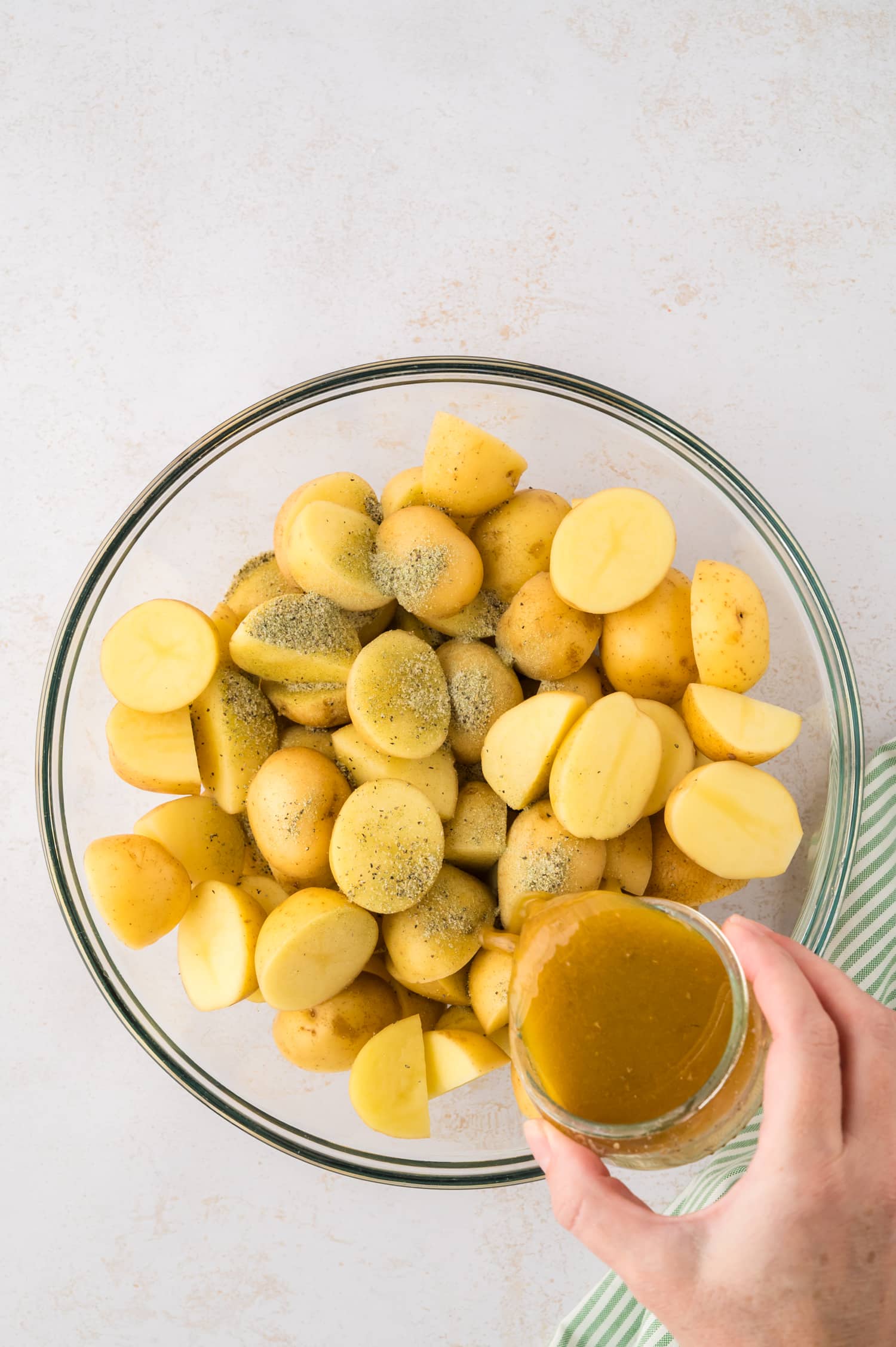 Oil and seasonings being poured onto raw potatoes