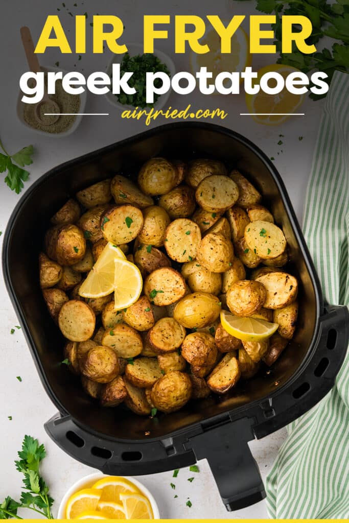 An air fryer basket full of greek potatoes and lemon slices