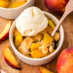 A close-up shows a mini peach cobbler with a spoon dipping A close-up shows a mini peach cobbler with a spoon dipped into it, and a scoop of vanilla ice cream resting on top of the warm cobbler.