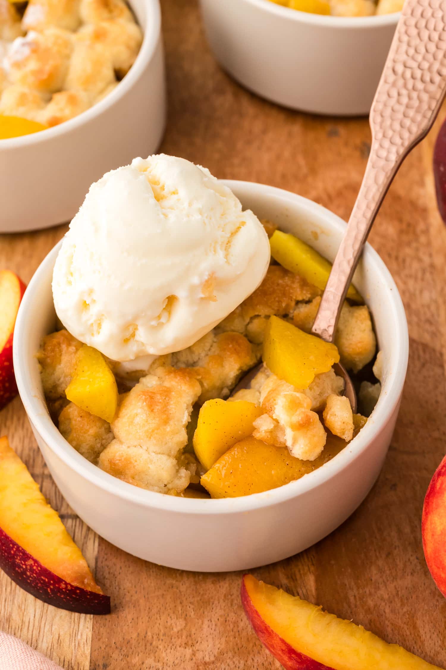A close-up shows a mini peach cobbler with a spoon dipping into it, revealing the soft peach filling underneath the golden topping.