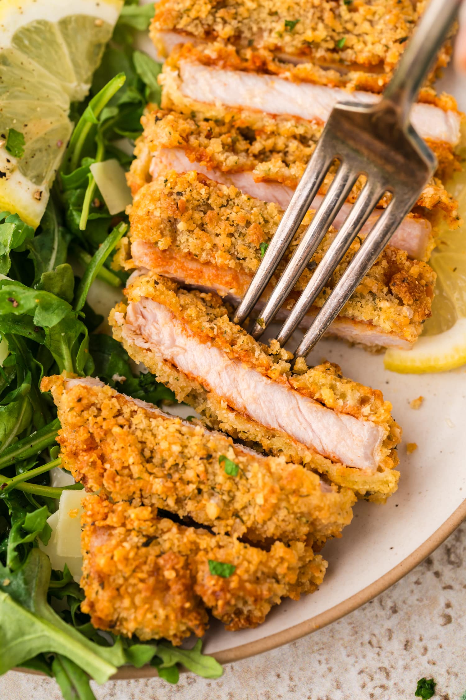 A close-up shows a fork pressing into a piece of pork milanese, and you can see the firm, crisp outside as the fork lifts the slice.