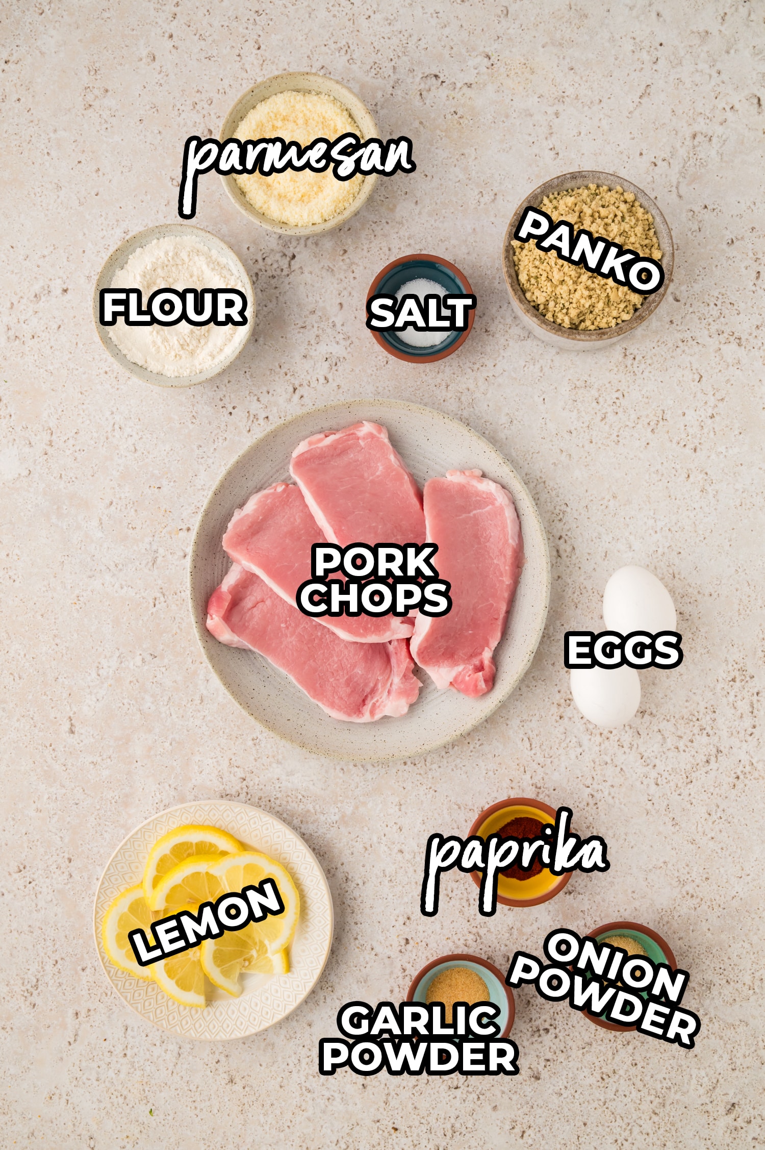 The ingredients for pork milanese are laid out on a countertop, each clearly labeled—including items like pork cutlets, breadcrumbs, flour, eggs, and seasonings—spanning the whole surface.