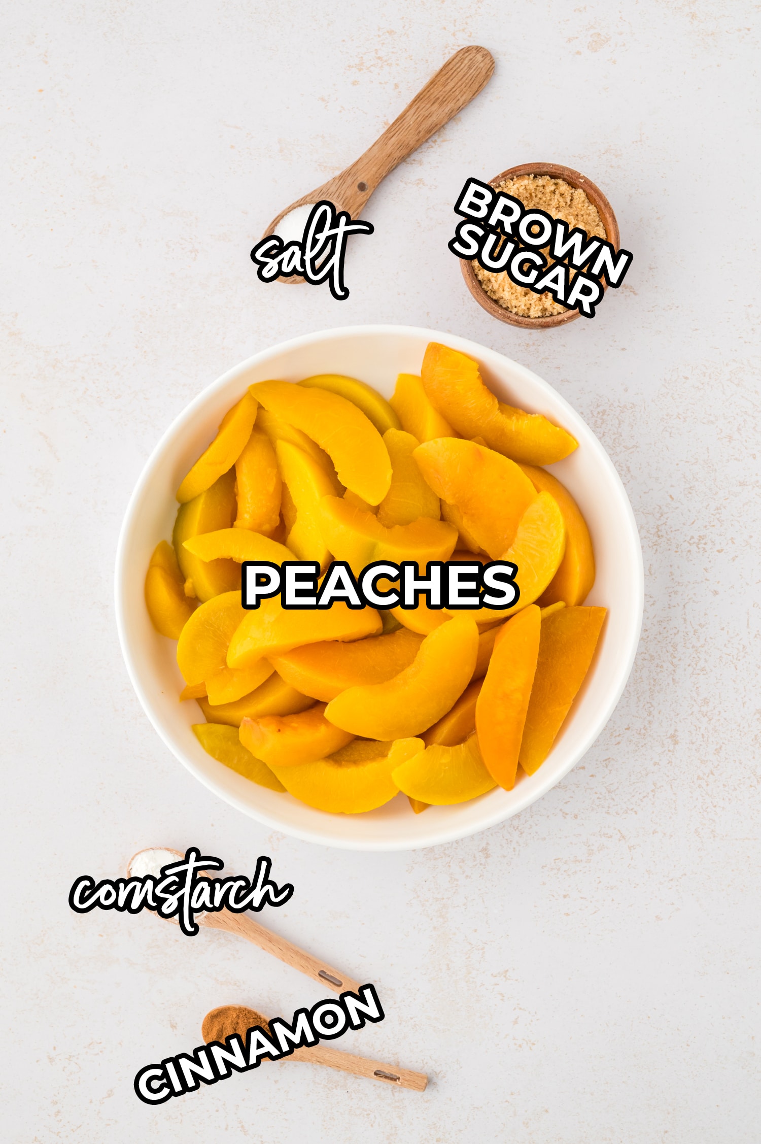 Sliced peaches, cornstarch, cinnamon, brown sugar, and salt are each in separate labeled containers, spread out on a white countertop, ready to be combined for the cobbler filling.