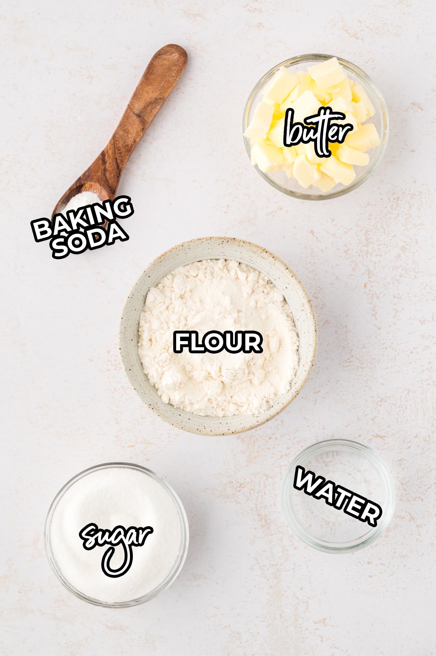 Sugar, butter, flour, water, and baking soda are each placed in separate labeled containers, arranged neatly on a white countertop, ready for use in the recipe.