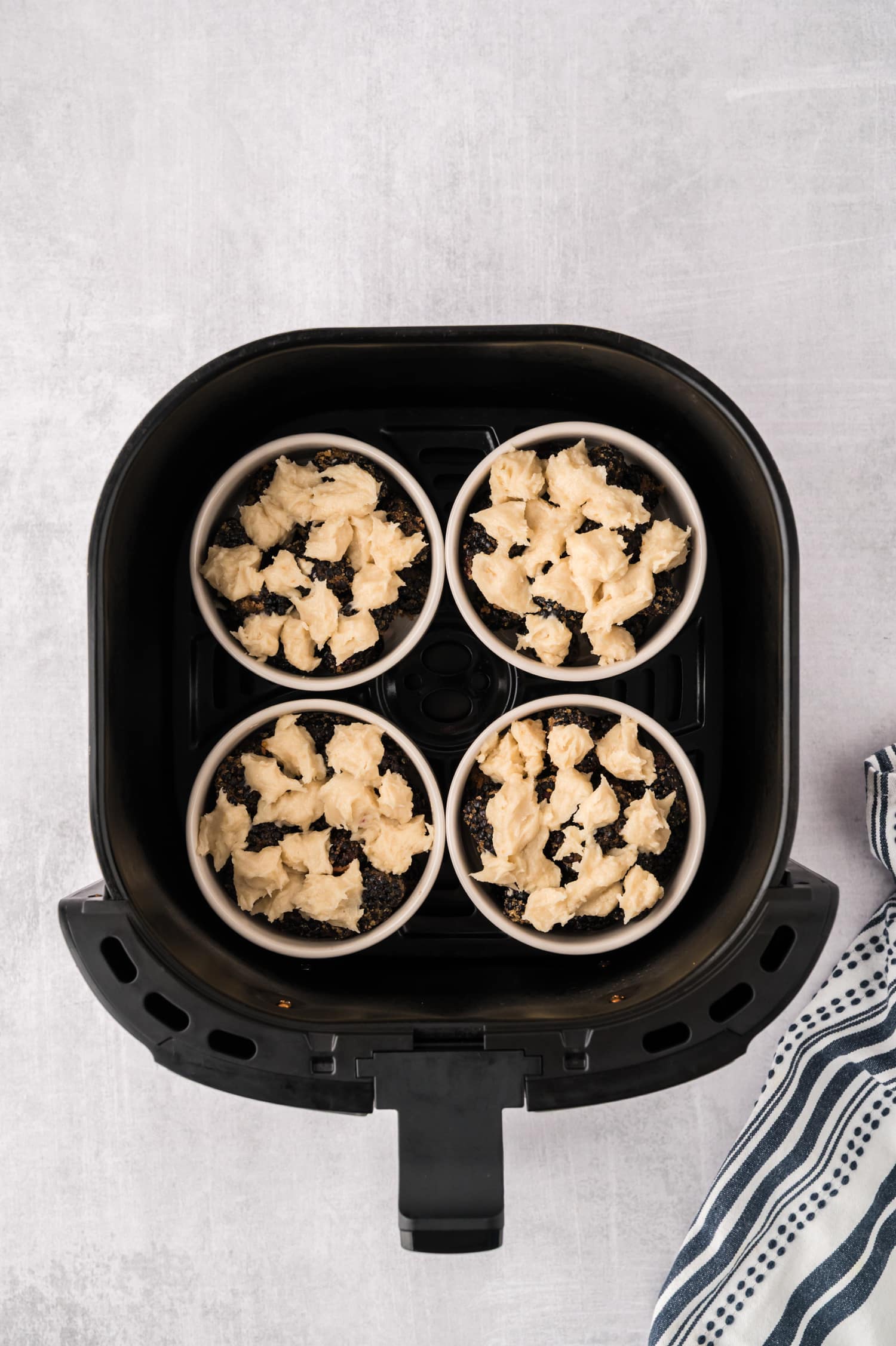 Four ramekins of uncooked blackberry cobbler inside an air fryer basket.