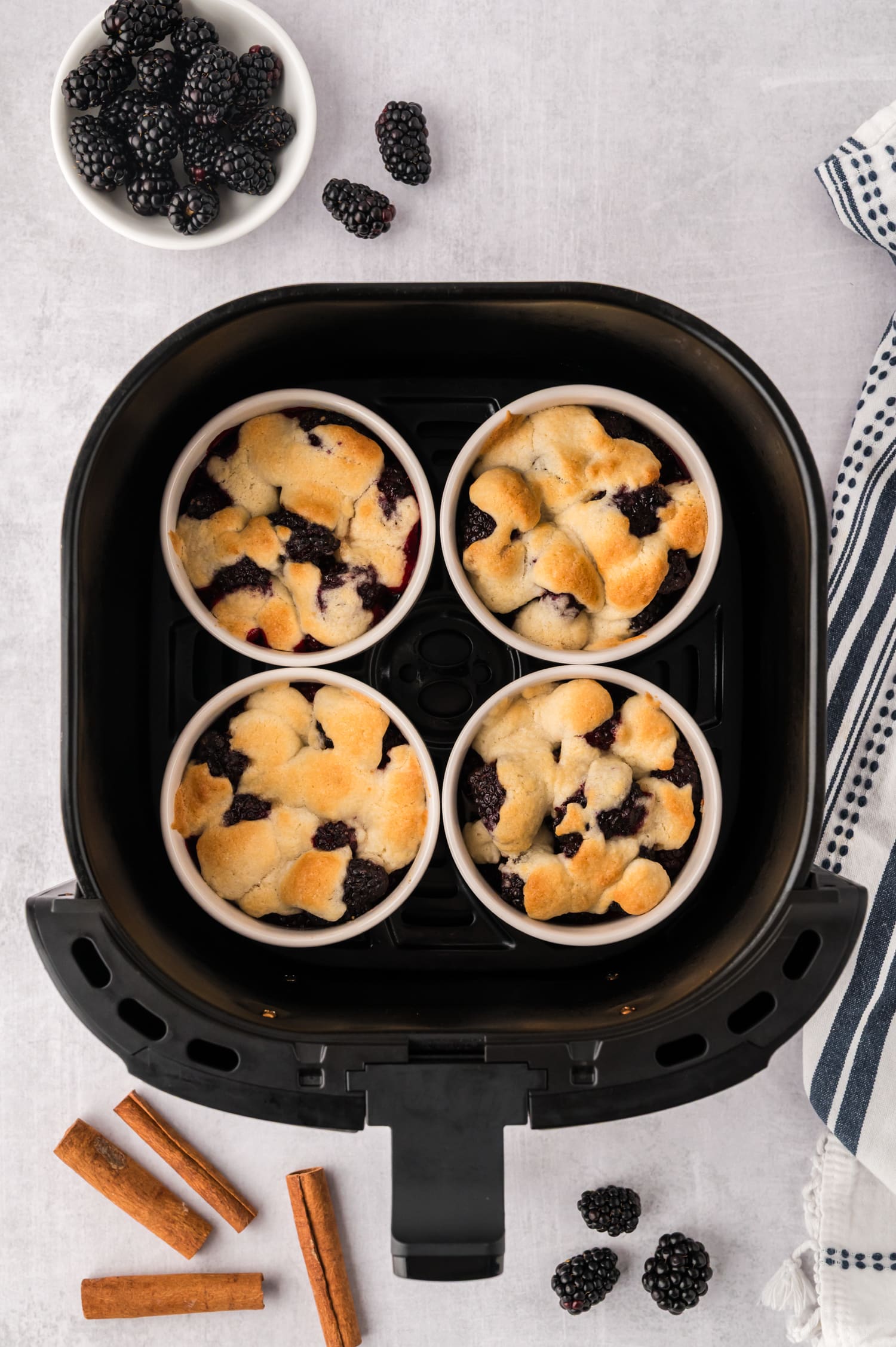 Four ramekins full of cooked blackberry cobbler in an air fryer basket.