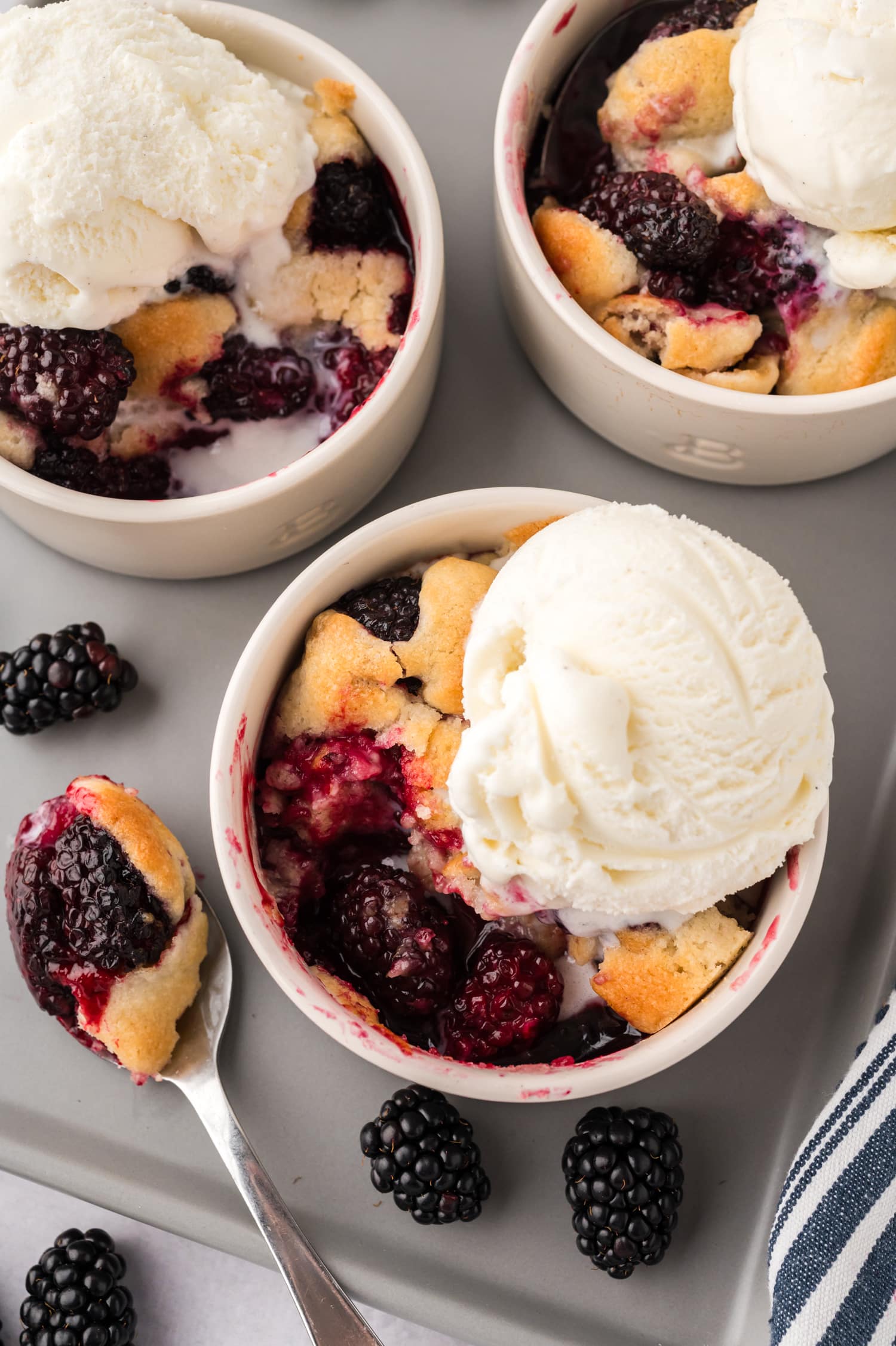 Close-up of a ramekin of blackberry cobbler with ice cream on top, with a bite scooped out.