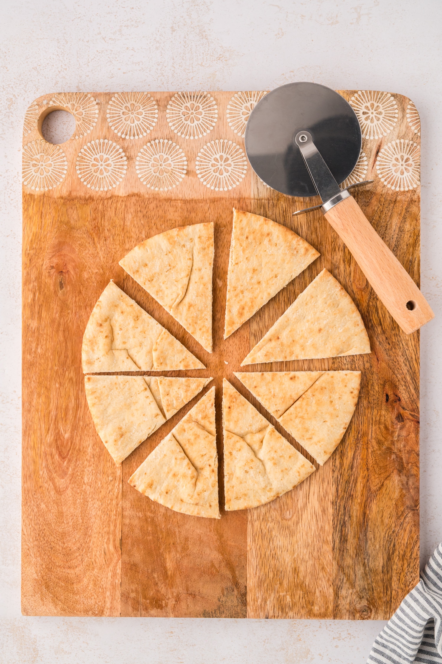 A pizza cutter resting next to a sliced pita cut into triangles.